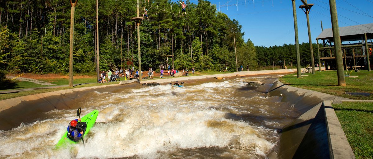 People kayaking on manmade whitewater river with ropes courses above the water