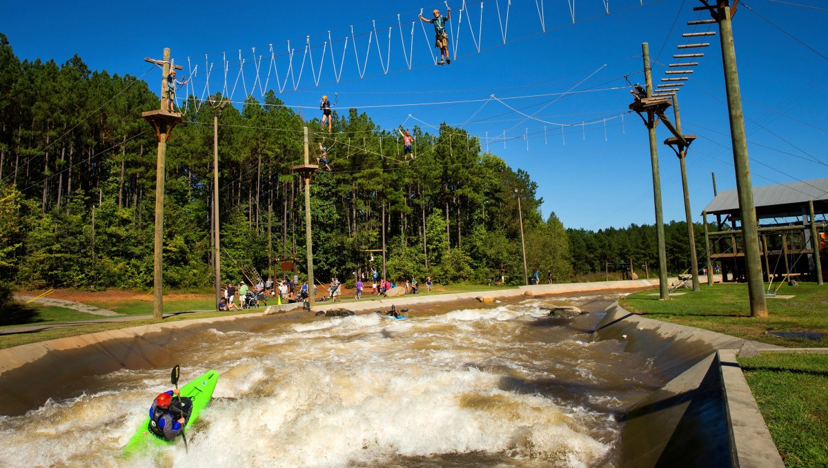 People kayaking on manmade whitewater river with ropes courses above the water