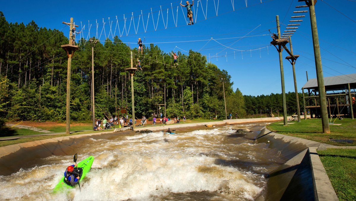 People kayaking on manmade whitewater river with ropes courses above the water