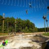 People kayaking on manmade whitewater river with ropes courses above the water