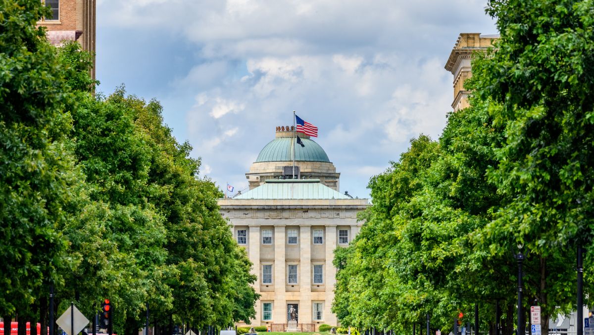North Carolina State Capitol building with trees  and American flag during daytime