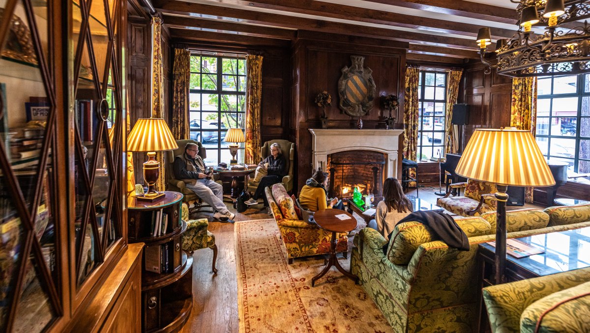 People sitting inside cozy cottage lobby with fire roaring in fireplace.