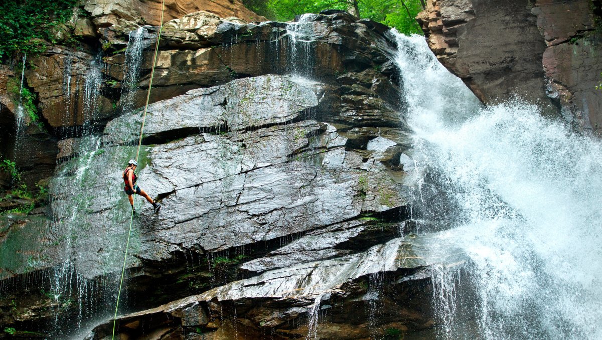 Person rappelling down waterfall as water cascades around them.