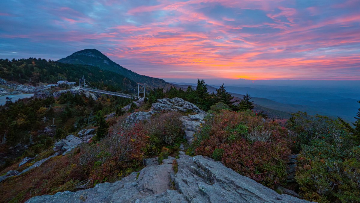 Aerial of Grandfather Mountain's Mile High Swinging Bridge during fall with bright sunset in distance