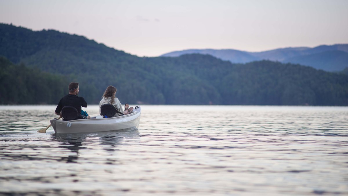 Couple canoeing on calm Lake James on cloudy day with mountains in distance.