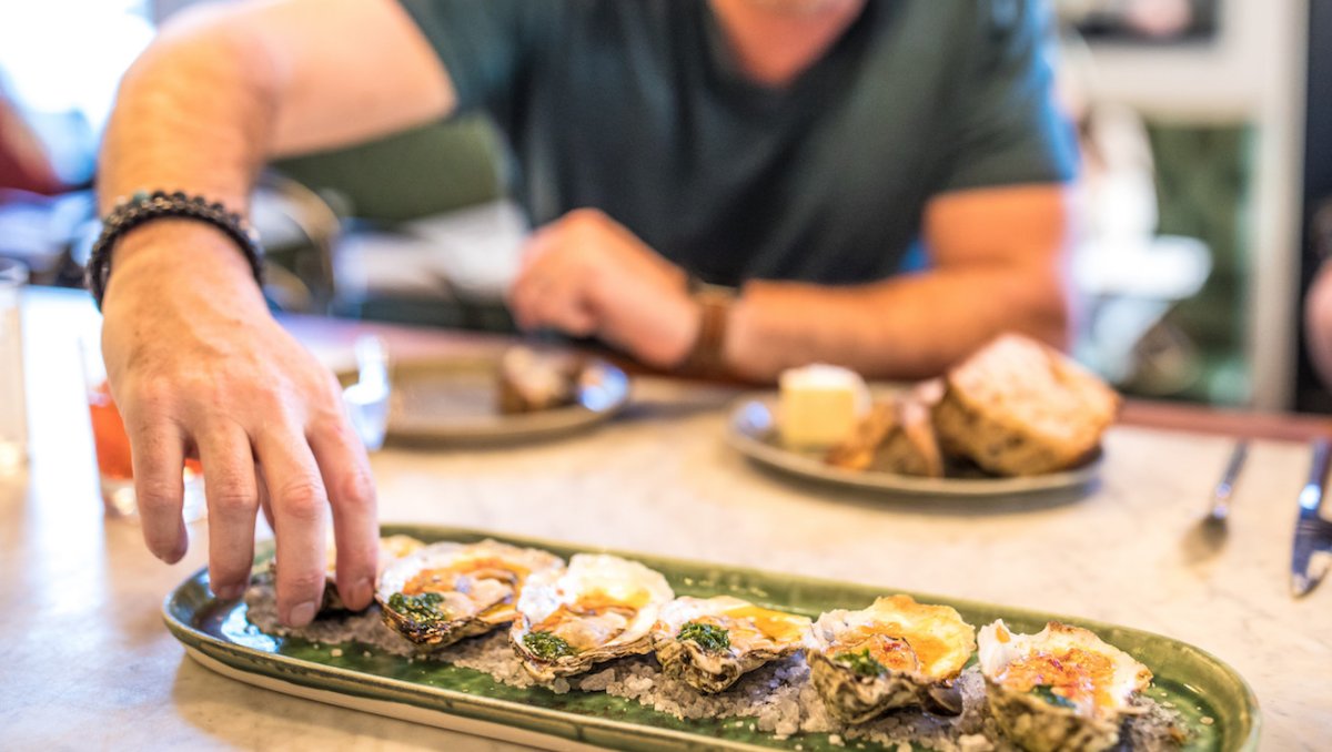 Man reaching for oyster on long plate while sitting at bar