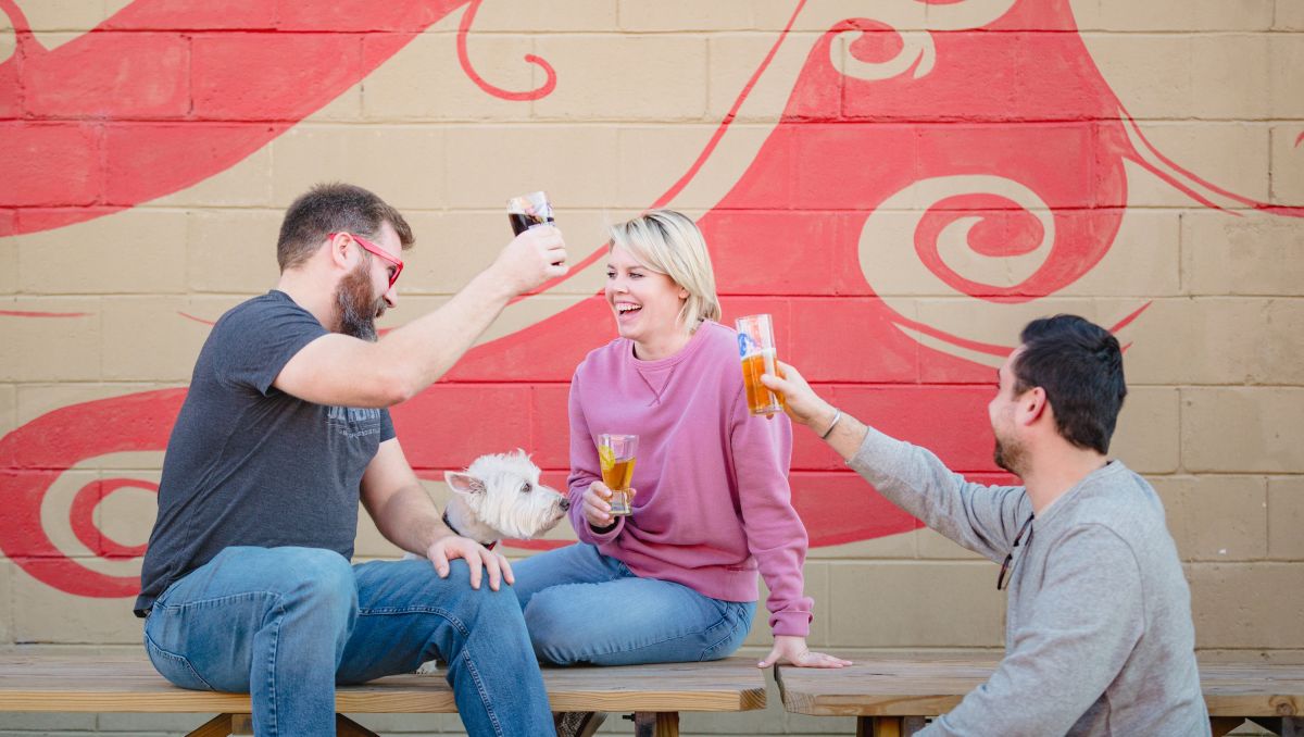 Friends sitting on a table toasting one another with beers at Mother Earth Brewing