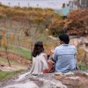 Couple sitting on rock sipping wine overlooking vineyard in fall