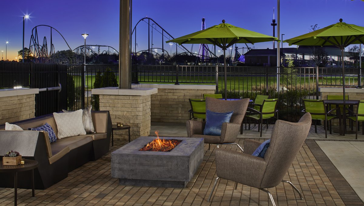 Outdoor patio and firepit with roller coasters in background at dusk.