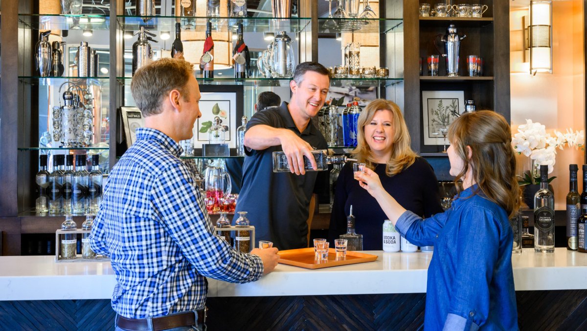 Smiling man and woman pouring a shot of liquor into shot glass woman is holding on other side of bar