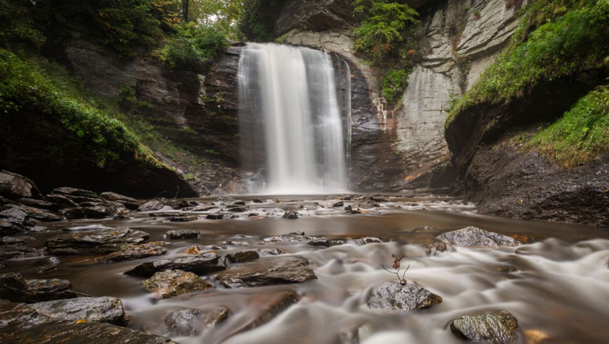 Waterfall cascading into stream with rocks surrounded by mountain walls