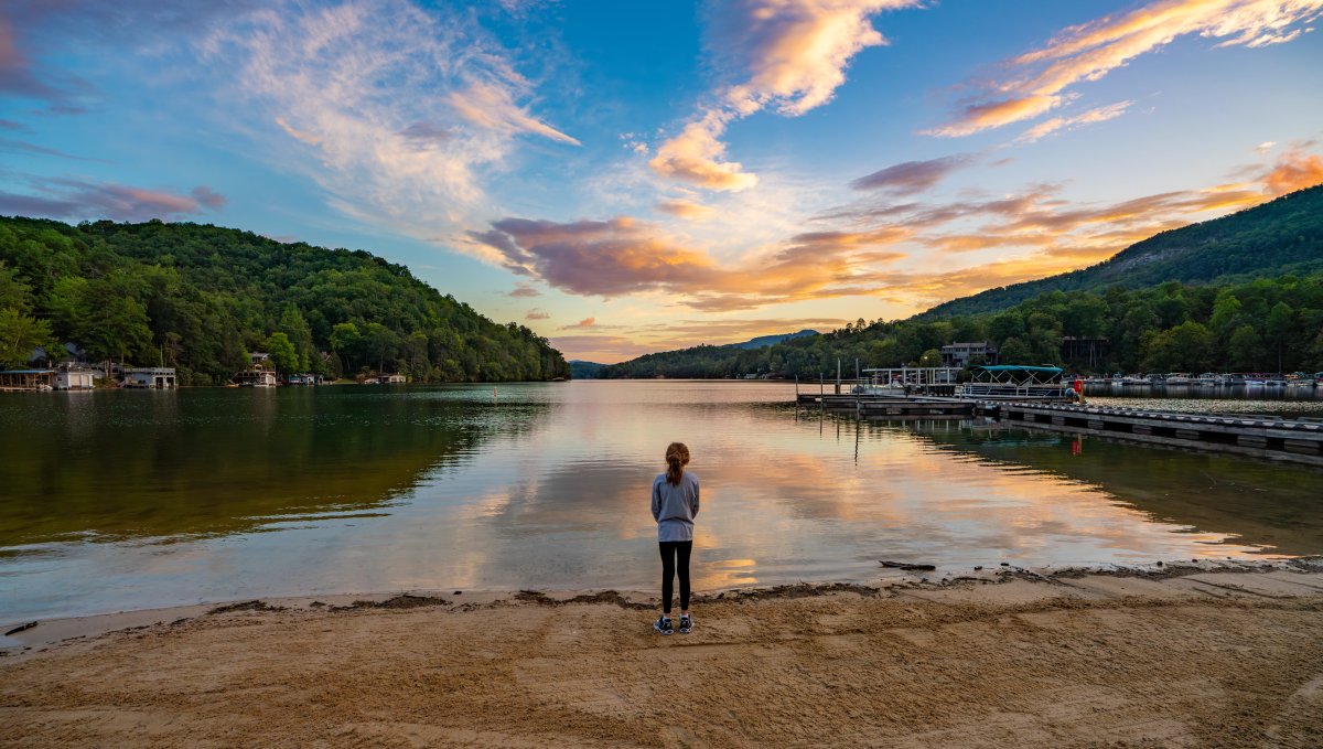 Child standing at edge of lake's beach with calm water, dock and shoreline in distance