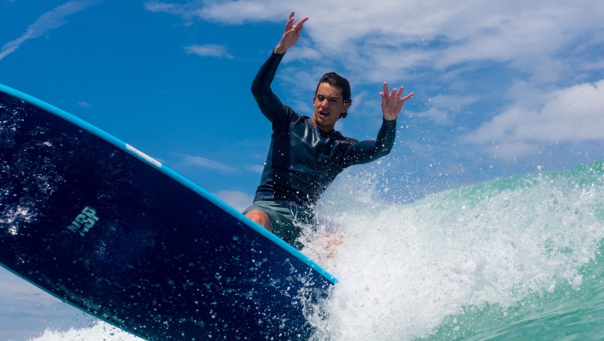 A man skillfully rides a surfboard atop a vibrant, crashing wave under a clear blue sky.