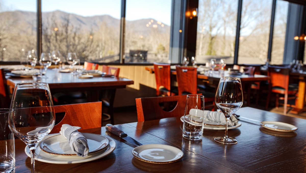 Dining room set with pretty plates and glassware with mountains through windows in background.