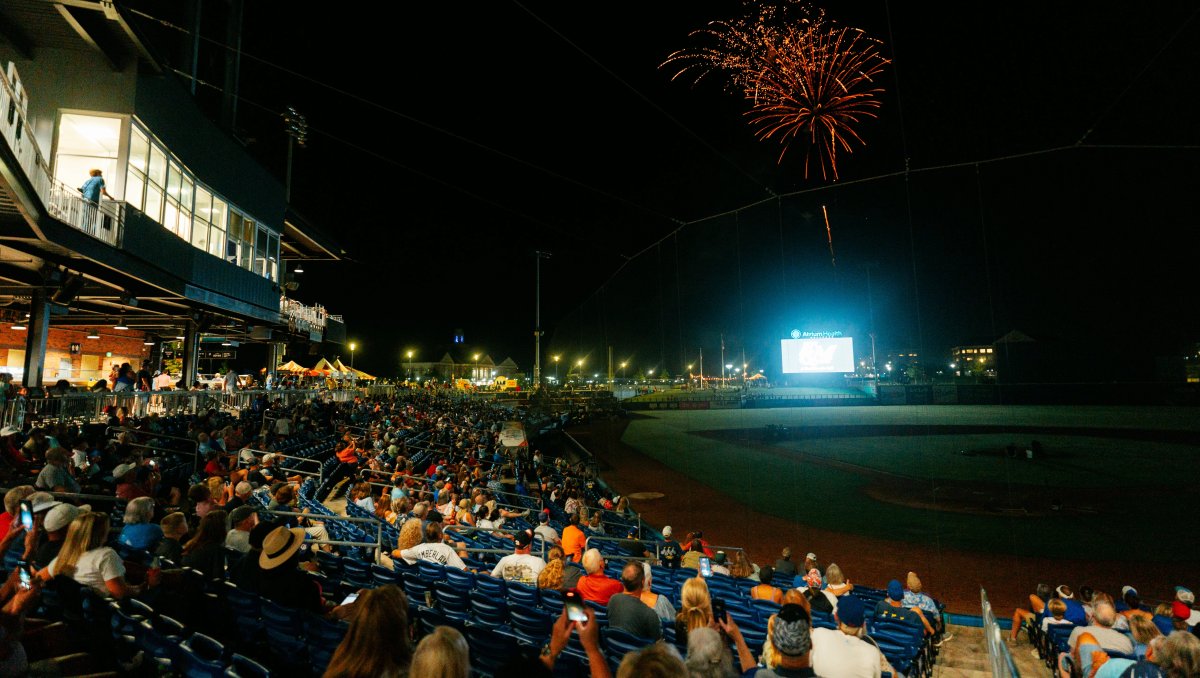 Fireworks over baseball field and crowd of people at nighttime