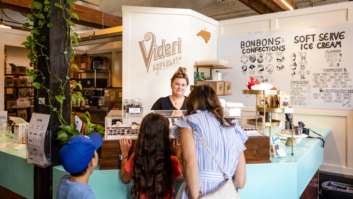 Mom and children picking out chocolate from display while employee waits behind Videri Chocolate counter.