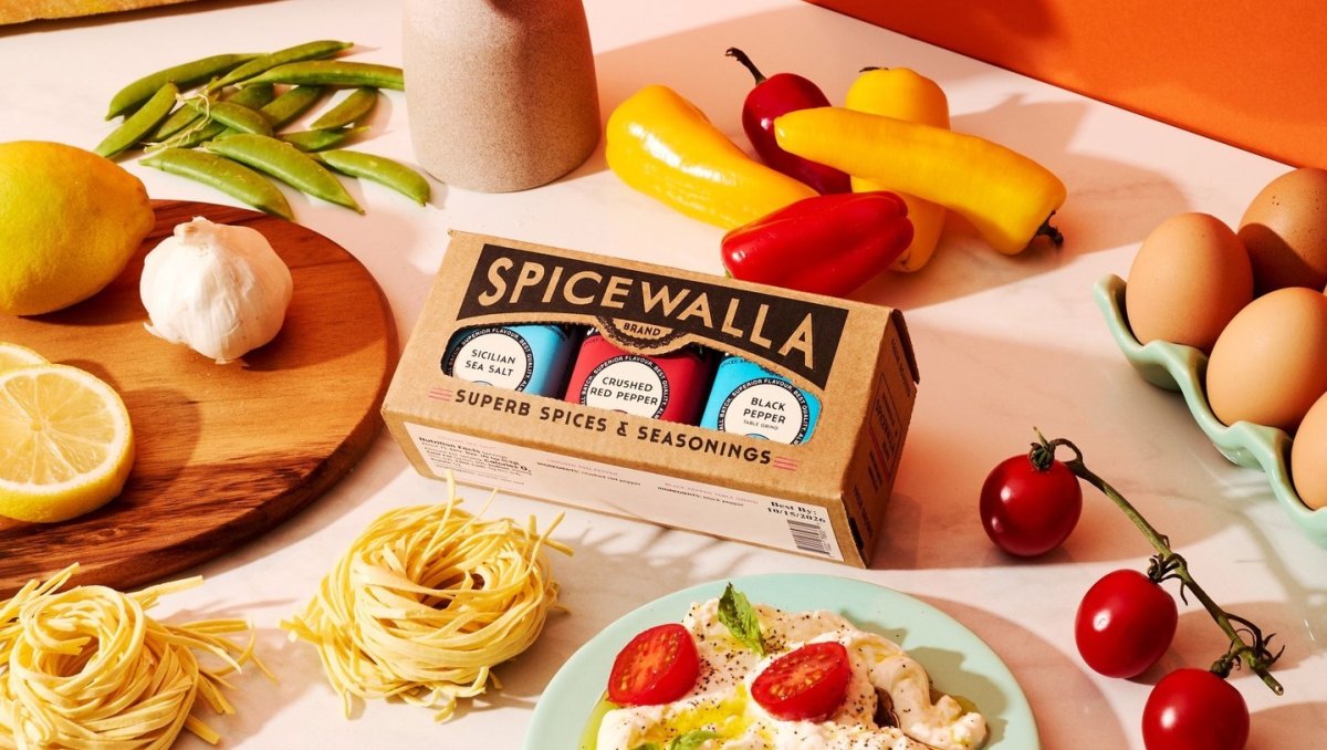 Spicewalla spices on display surrounded by tomatoes, peppers and other foods.
