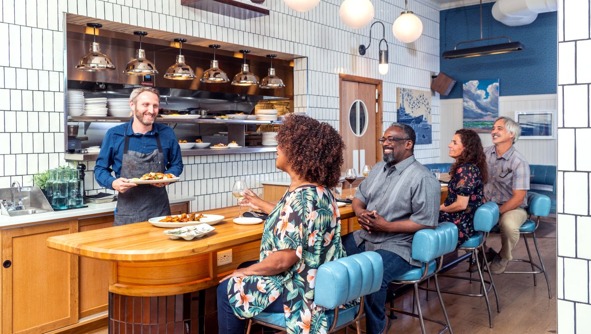 Four people sitting at bar in restaurant with waiter serving food