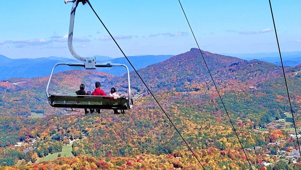 People riding ski lift down mountain with mountains covered in fall foliage in background