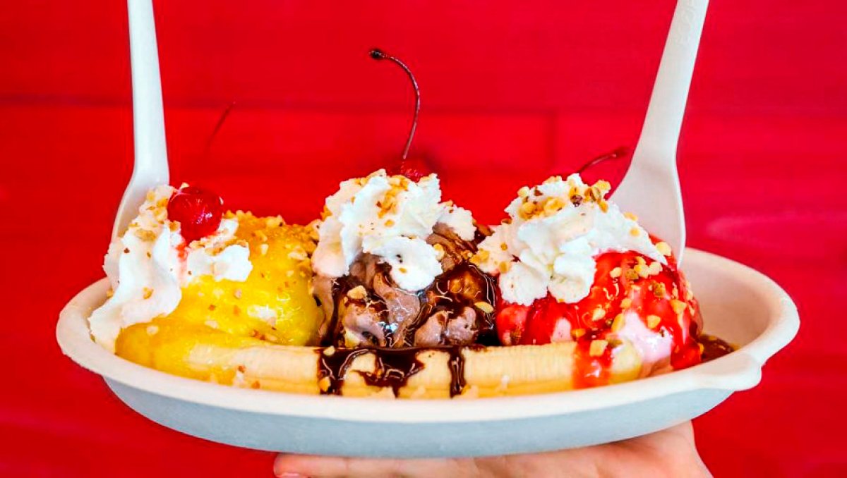 Close-up of ice cream sundae being held up against red wall.