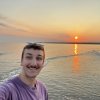 Young man taking selfie on beach with sun setting over water in background