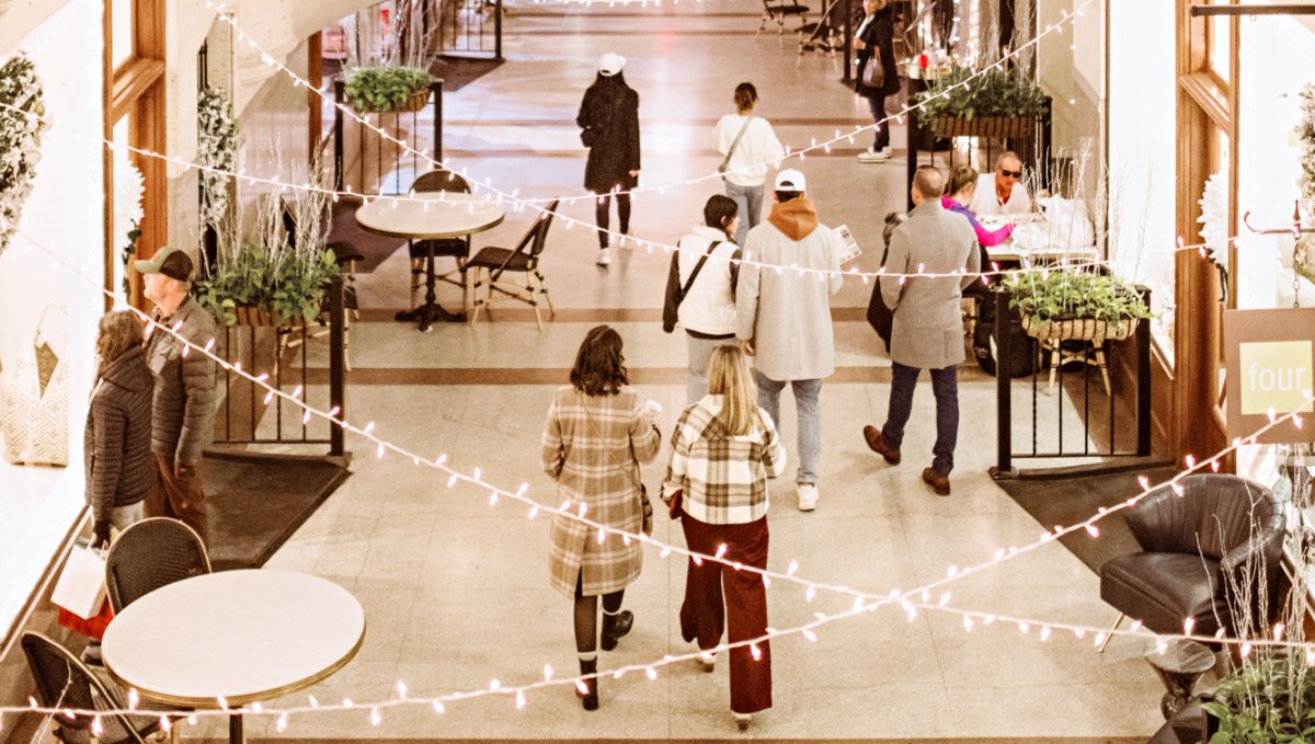 People shopping in intimate mall area of building, surrounded by plants, lights and beautiful architecture.