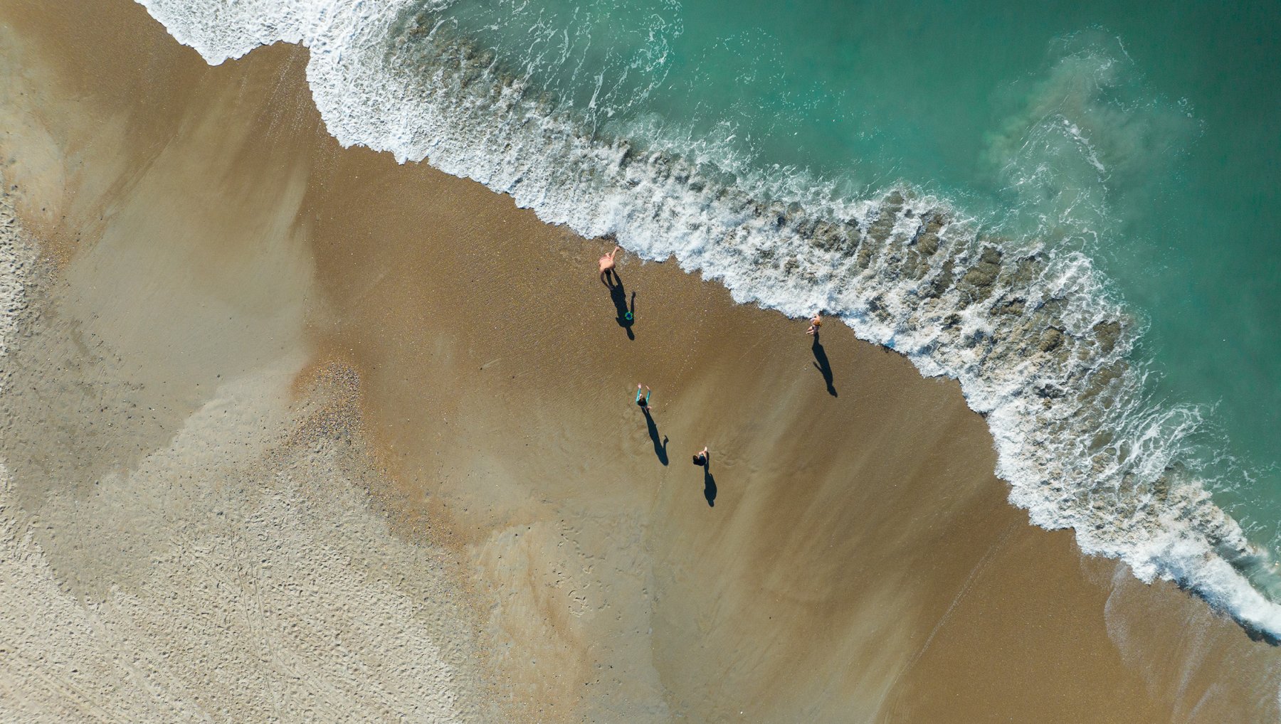 Aerial of family playing in waves on empty beach
