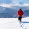 Back of person in red jacket walking through snow with Blue Ridge Mountains in background