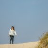 Woman walking on sand with dunes to the right and blue sky in background