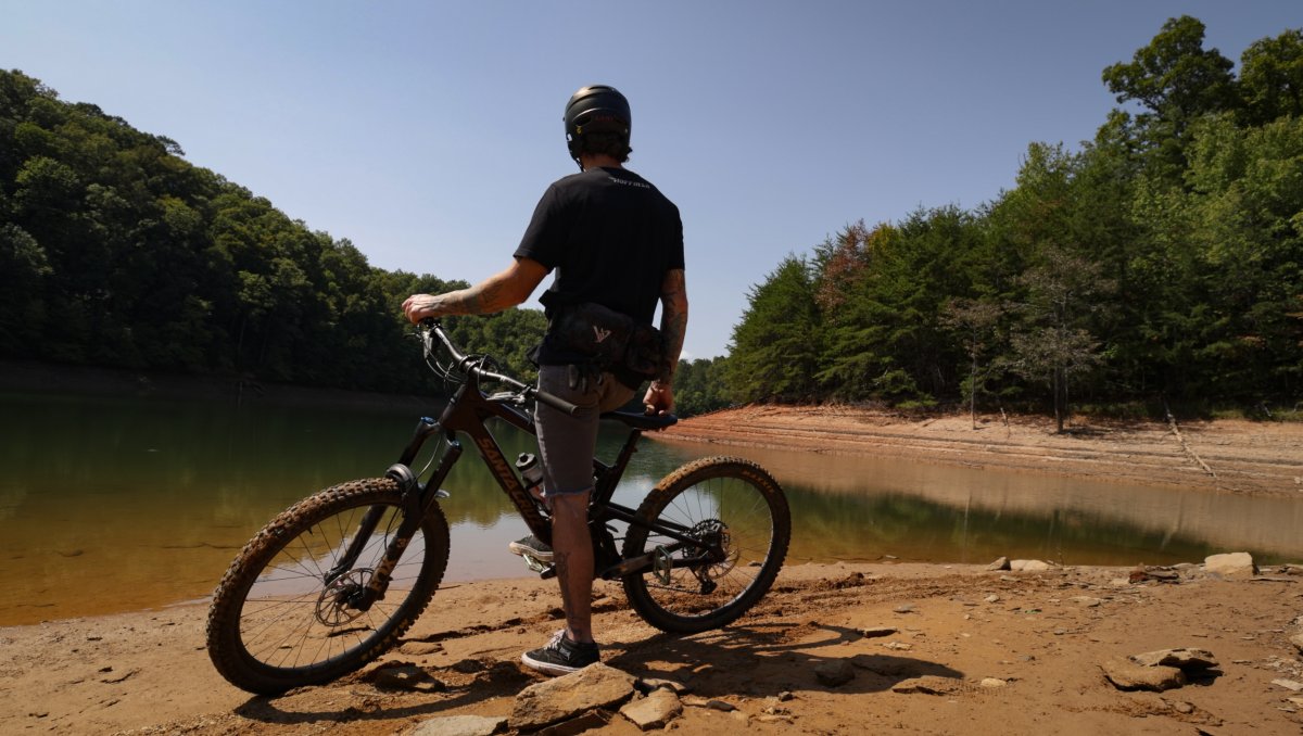 Back of man on mountain bike admiring lake in mountains during daytime.