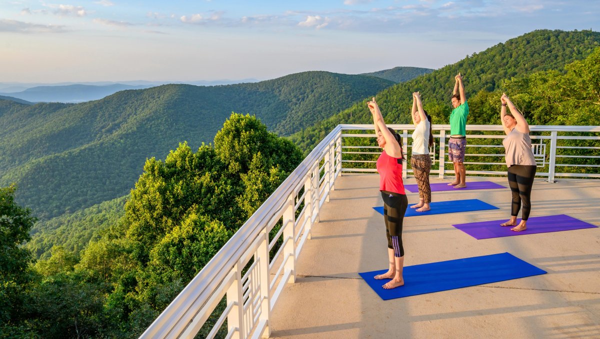 Four people doing yoga while overlooking green mountains and hills