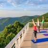 Four people doing yoga while overlooking green mountains and hills