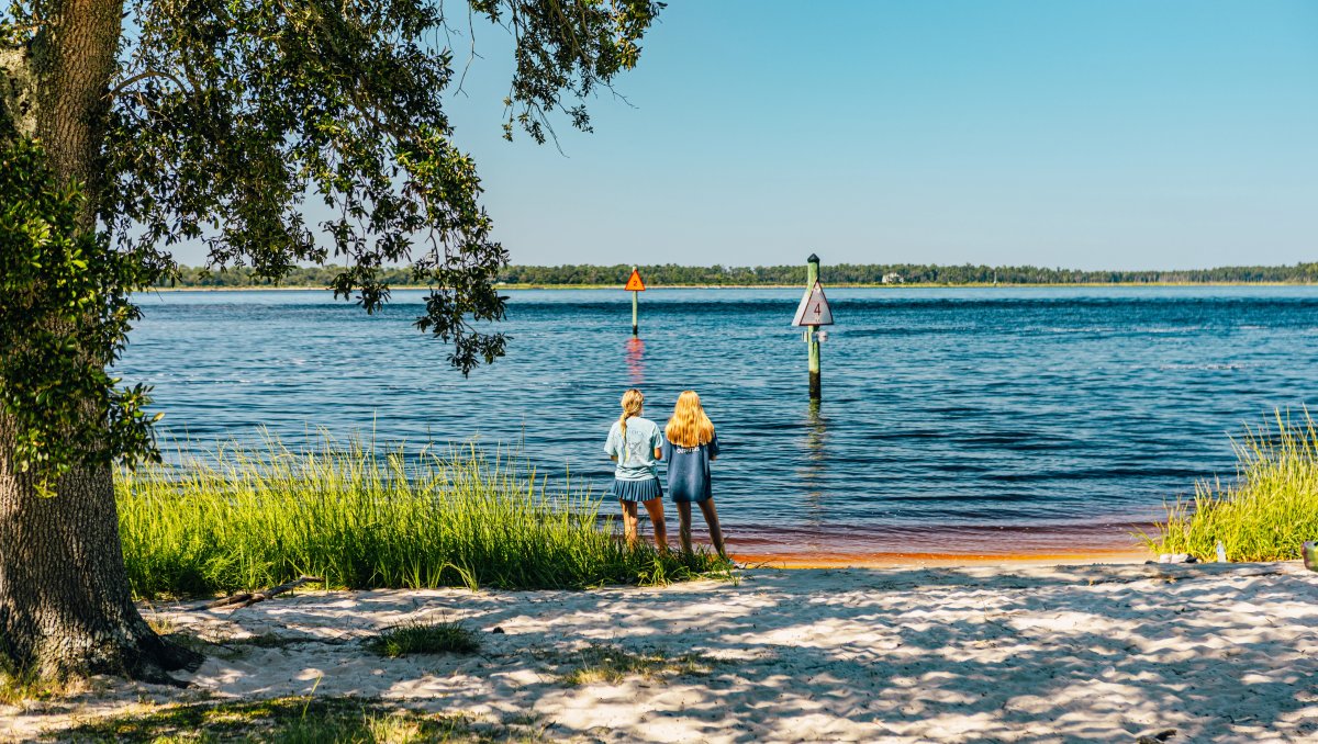 Two girls standing at edge of water at state park with shoreline in far distance