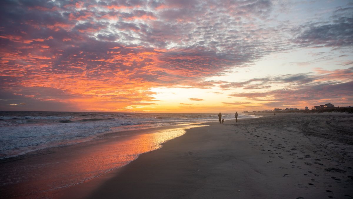 Couple walking in distance on empty Atlantic Beach at sunset