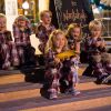 6 small children sit on wooden steps smiling in matching pajamas as one holds gold Polar Express ticket