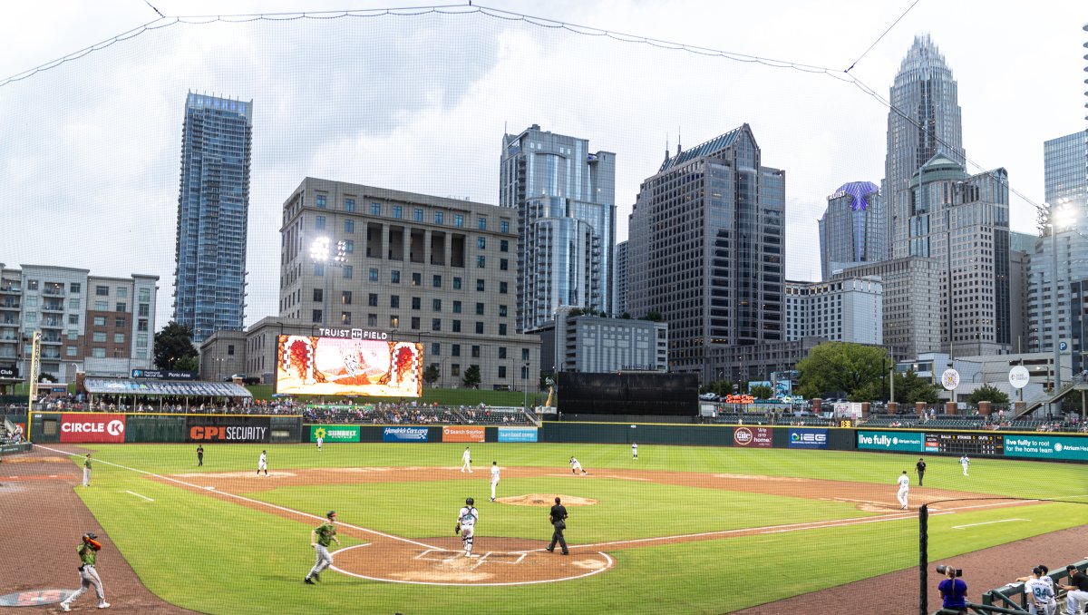 Teams playing baseball game at Truist Field with Charlotte skyline in background. 