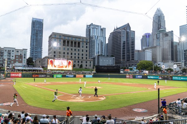 Teams playing baseball game at Truist Field with Charlotte skyline in background. 