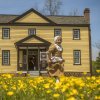 Child dressed in 1700s period garb running in field of yellow flowers in front of historic building