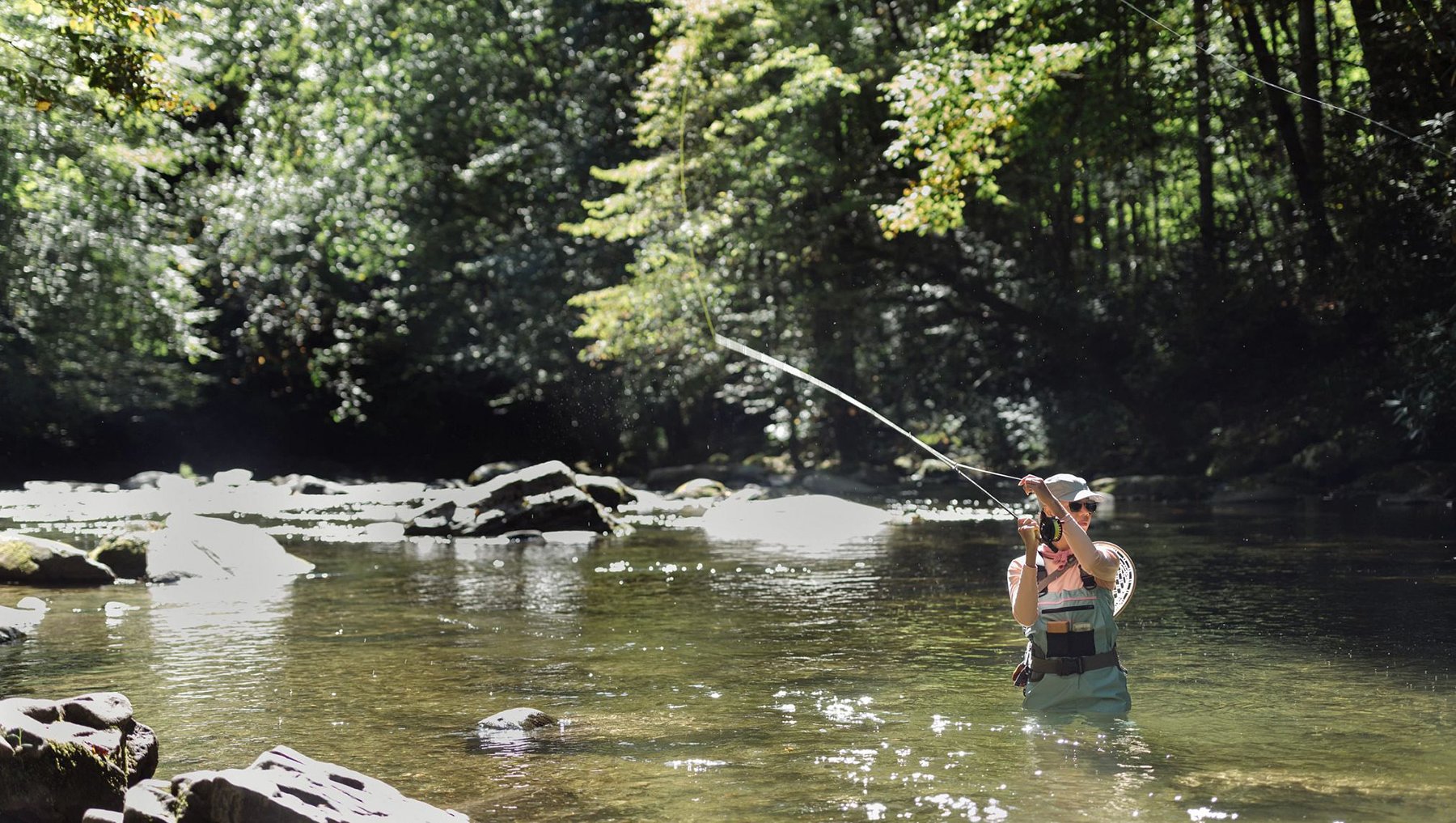 Action shot of woman casting a line out on her fly rod in a river in Bryson City.