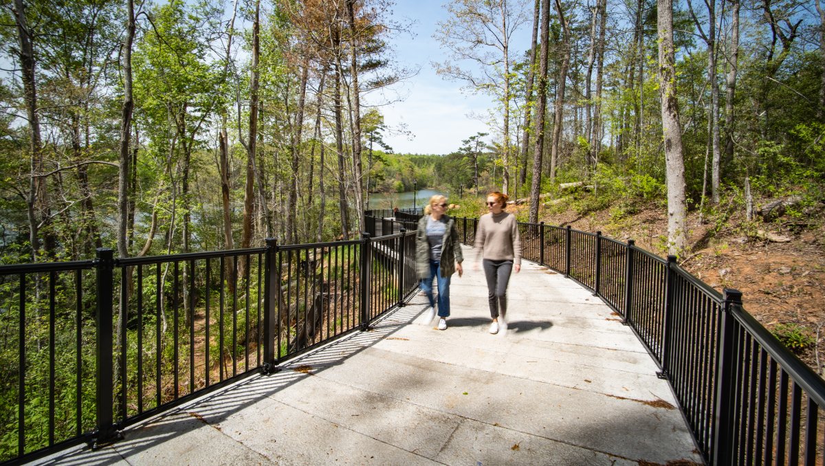 Two women walking on paved River Walk surrounded by trees