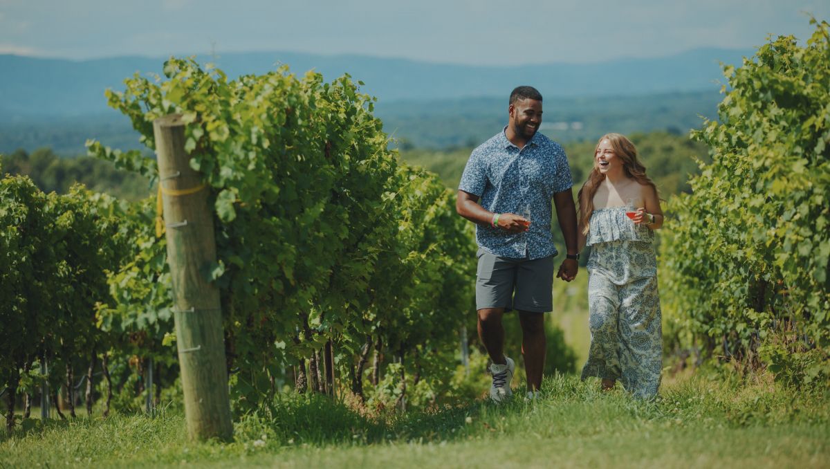 Smiling couple walking hand in hand through Raffaldini Vineyards' vineyard on sunny day