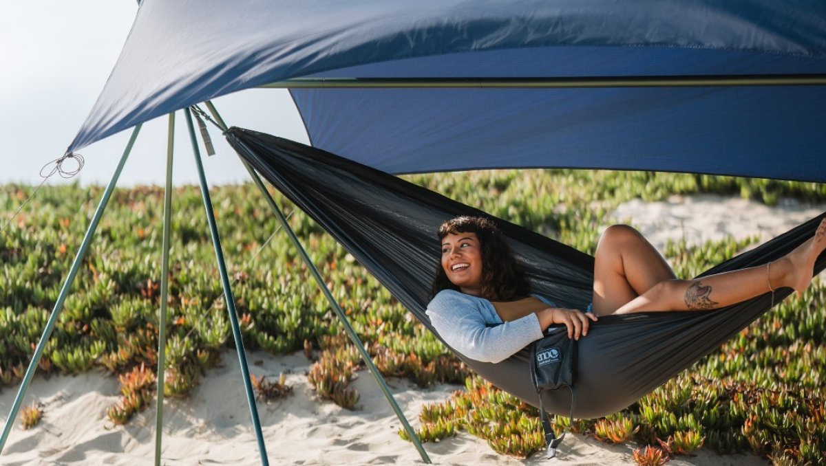 A woman peacefully rests in a hammock on the beach, soaking up the sun and the serene coastal atmosphere