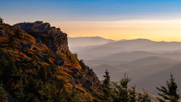 Linville Peak surrounded by green trees and Blue Ridge Mountains in distance