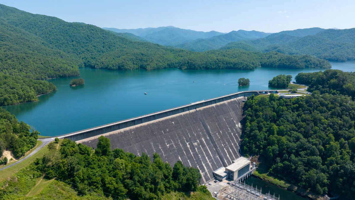 Aerial are large dam surrounded by mountains and green trees during daytime