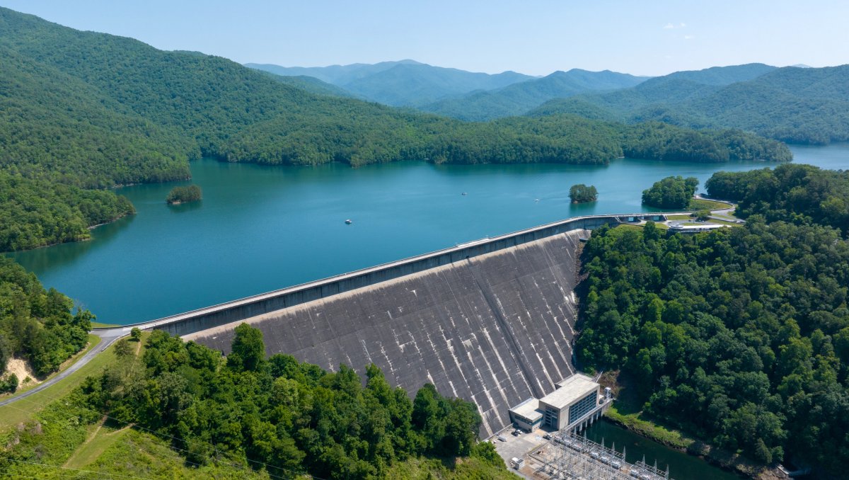 Aerial are large dam surrounded by mountains and green trees during daytime