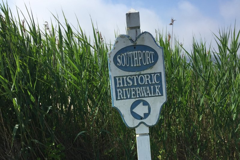 Sign reading Southport Historic Riverwalk in front of tall green grass