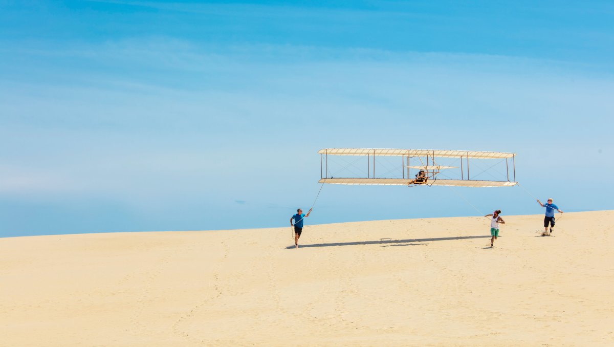 People assisting in getting hang glider off the ground on sand dune.