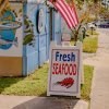 Sign that reads "Fresh Seafood" outside of blue shack.