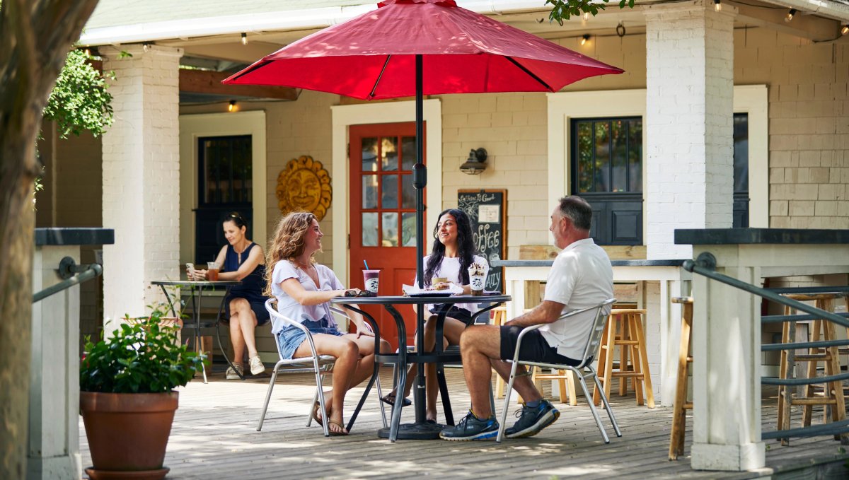 Three friends sitting on patio drinking coffee under red umbrella