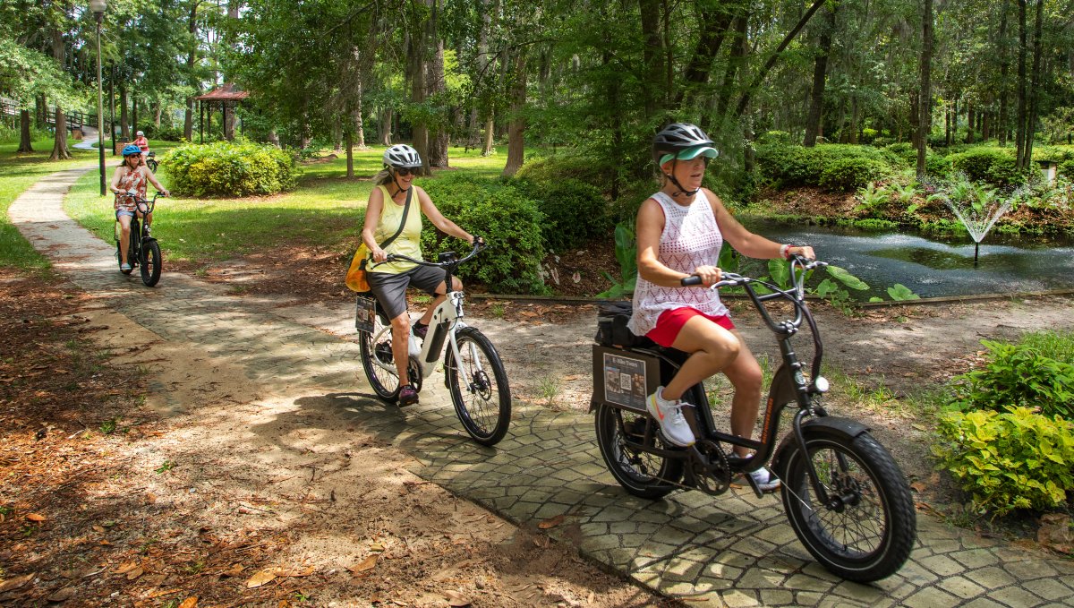 Friends riding bikes through beautiful park surrounded by trees in Wilmington.